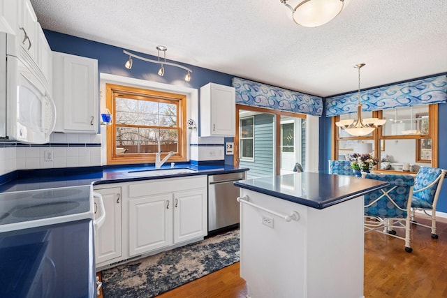 kitchen with a sink, white appliances, dark countertops, and wood finished floors