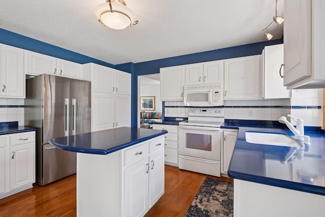 kitchen featuring dark wood finished floors, white appliances, dark countertops, and a sink