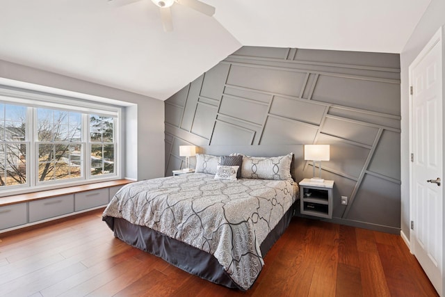 bedroom with a ceiling fan, dark wood-style floors, vaulted ceiling, and a decorative wall