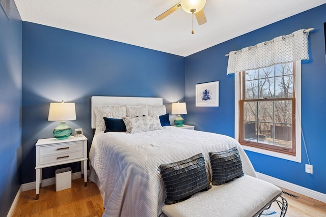 bedroom with visible vents, wood finished floors, baseboards, and ceiling fan