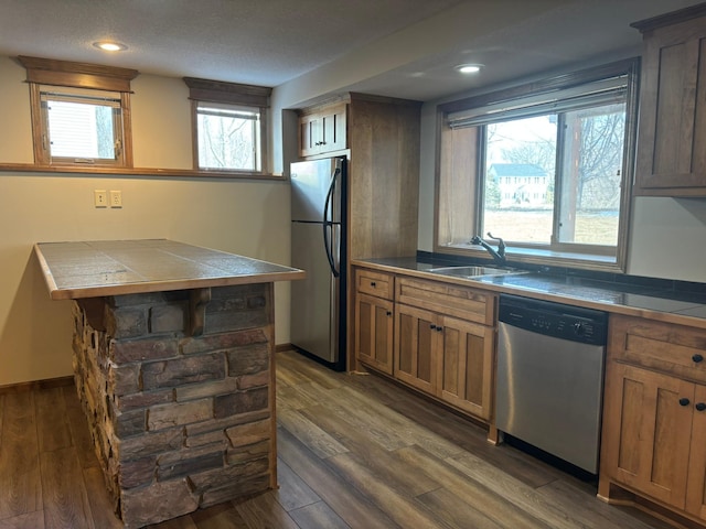 kitchen featuring baseboards, tile counters, dark wood-style floors, appliances with stainless steel finishes, and a sink