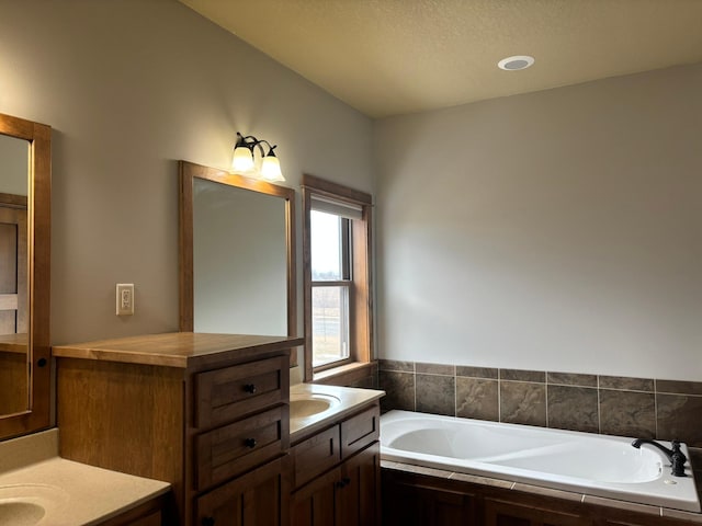 full bath featuring two vanities, a garden tub, and a sink