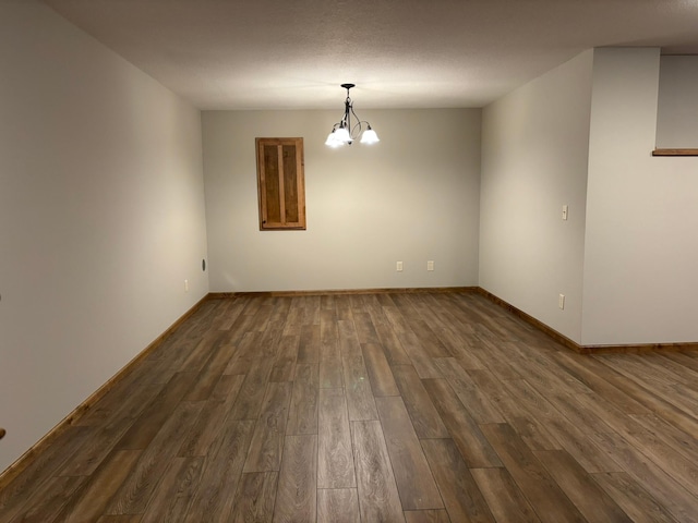 spare room featuring baseboards, a chandelier, and dark wood-type flooring