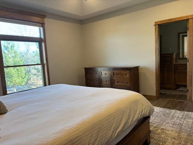 bedroom with ensuite bath, baseboards, and wood finished floors