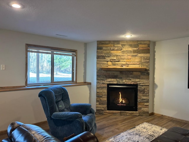 sitting room featuring a textured ceiling, a stone fireplace, baseboards, and wood finished floors