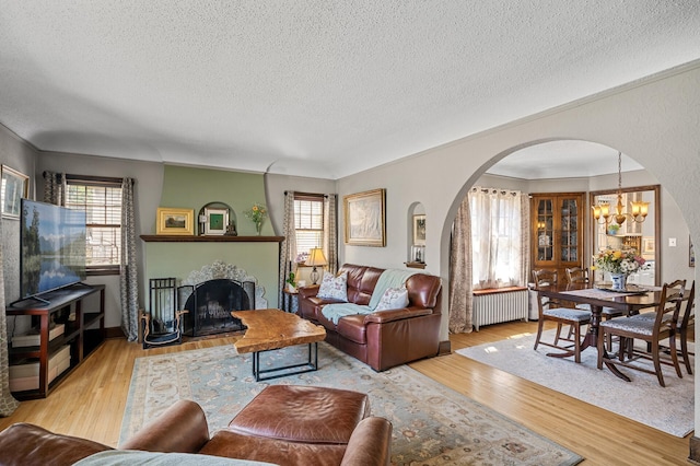 living area with wood finished floors, a notable chandelier, a textured ceiling, arched walkways, and radiator heating unit