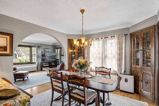 dining room featuring a textured ceiling, arched walkways, light wood-style floors, a chandelier, and radiator heating unit
