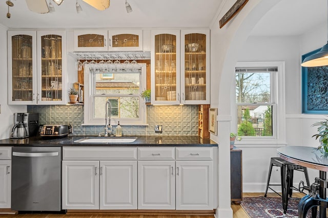 bar with decorative backsplash, stainless steel dishwasher, arched walkways, and a sink