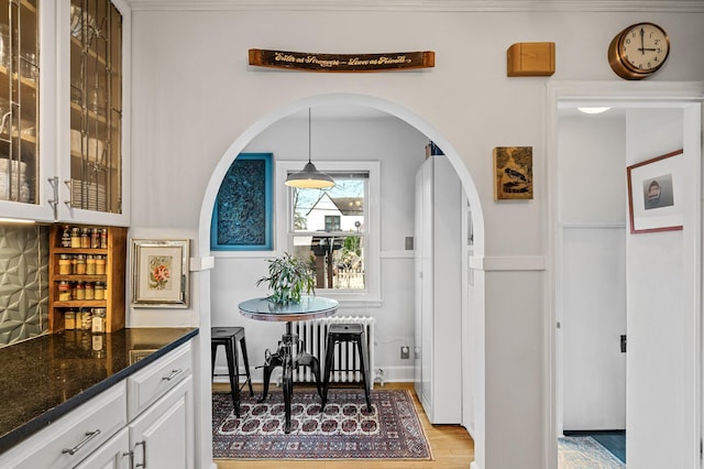 dining space with arched walkways, radiator heating unit, and light wood-type flooring