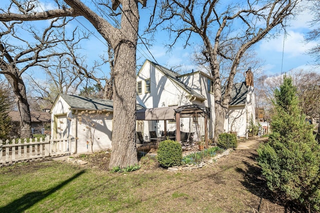 view of side of home with fence, stucco siding, a chimney, and a lawn