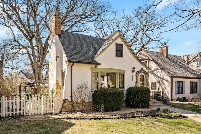 english style home with a front lawn, fence, and a chimney