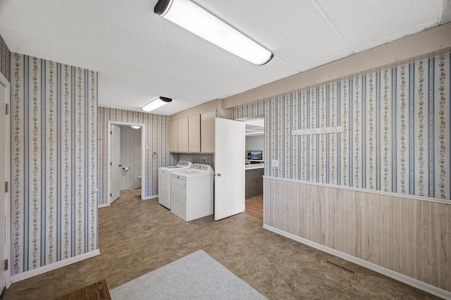 washroom featuring wallpapered walls, cabinet space, visible vents, a wainscoted wall, and washing machine and clothes dryer