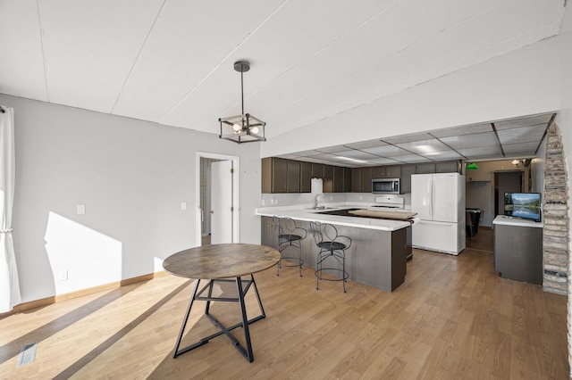 kitchen featuring stainless steel microwave, freestanding refrigerator, a peninsula, light wood-type flooring, and a sink