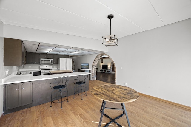 kitchen featuring arched walkways, light wood-style flooring, a peninsula, white appliances, and a sink