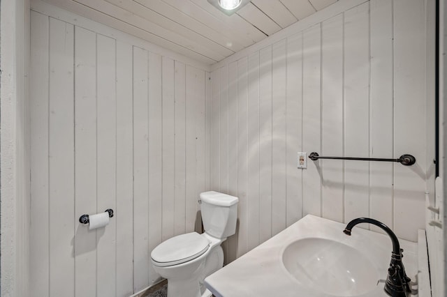 bathroom with wood walls, a sink, and toilet