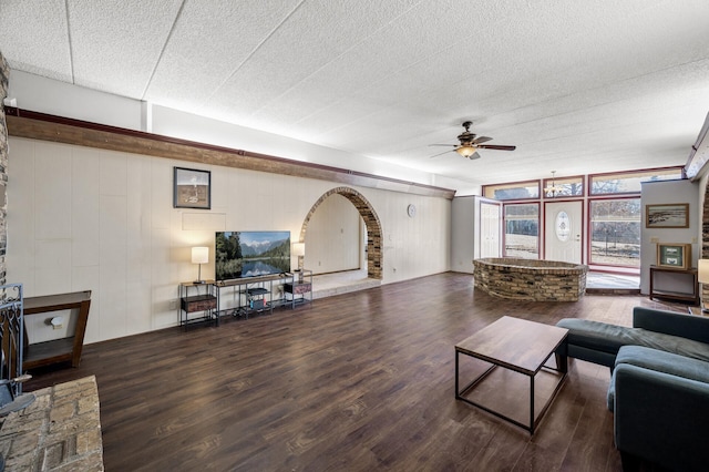 living room with ceiling fan, a textured ceiling, arched walkways, and wood finished floors