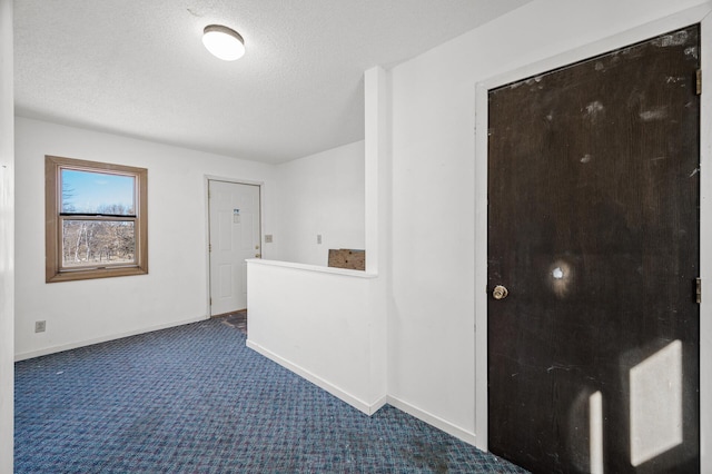 corridor with dark colored carpet, a textured ceiling, and baseboards