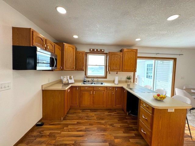 kitchen featuring a peninsula, dark wood-style flooring, a sink, brown cabinetry, and stainless steel microwave