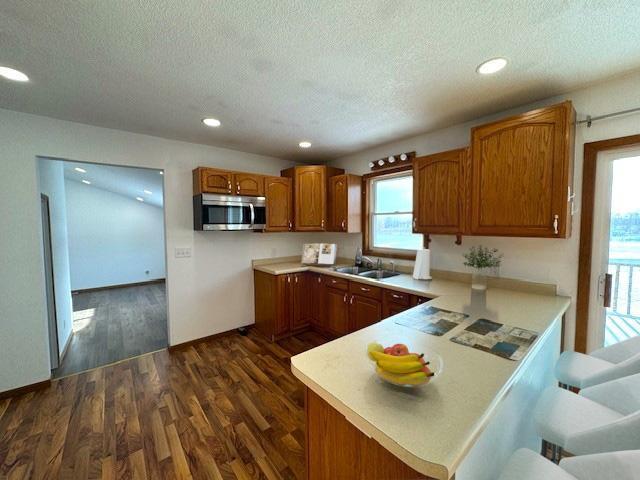 kitchen featuring a peninsula, stainless steel microwave, brown cabinets, and light countertops