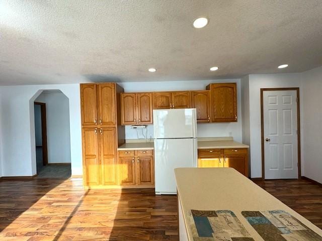 kitchen with dark wood-style floors, arched walkways, recessed lighting, freestanding refrigerator, and a textured ceiling