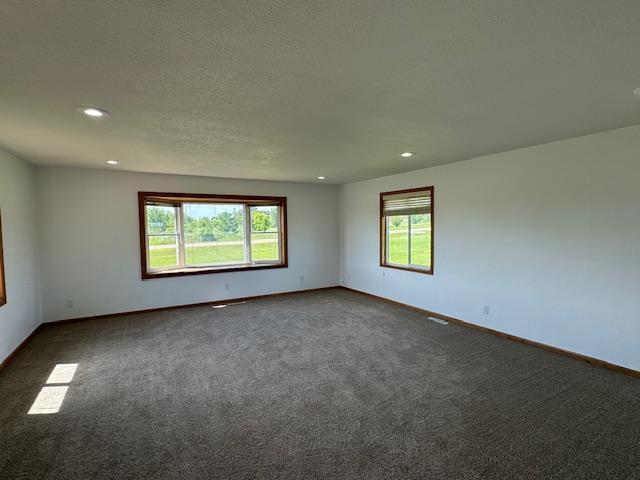 unfurnished room with baseboards, dark carpet, and a wealth of natural light