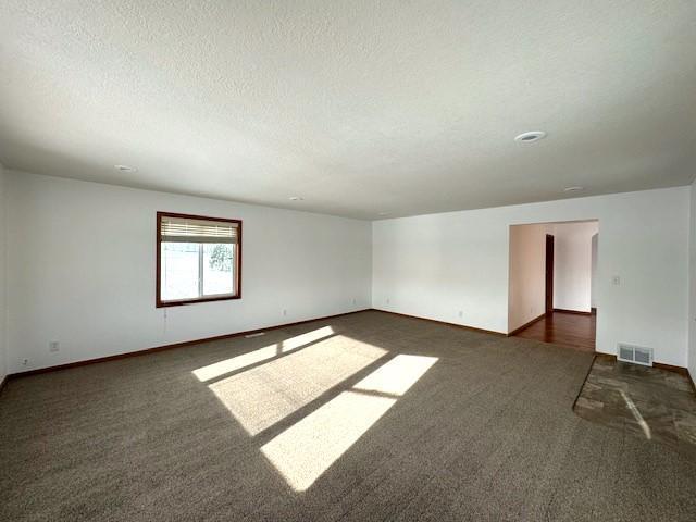 carpeted empty room with baseboards, visible vents, and a textured ceiling