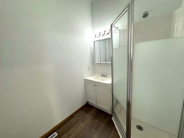 full bath with visible vents, vanity, a shower stall, wood finished floors, and baseboards