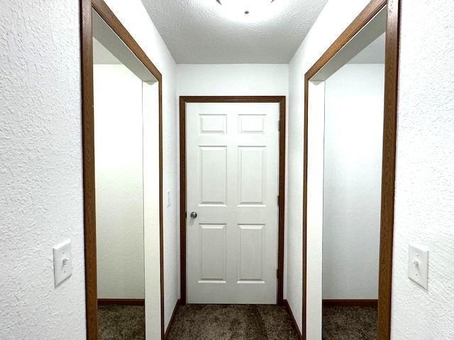 corridor with dark carpet, a textured ceiling, and a textured wall