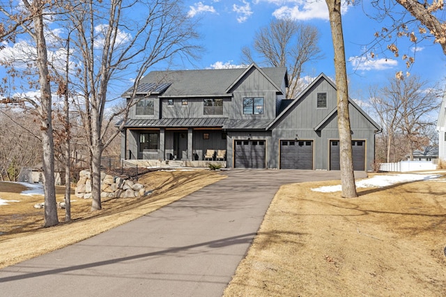 modern inspired farmhouse featuring a garage, roof mounted solar panels, a porch, and driveway