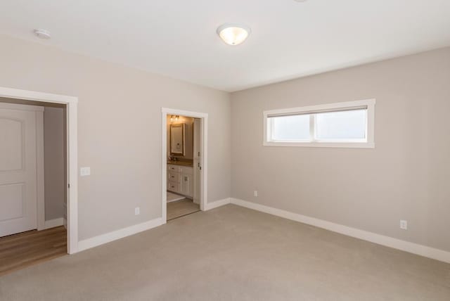 unfurnished bedroom with ensuite bath, baseboards, and light colored carpet