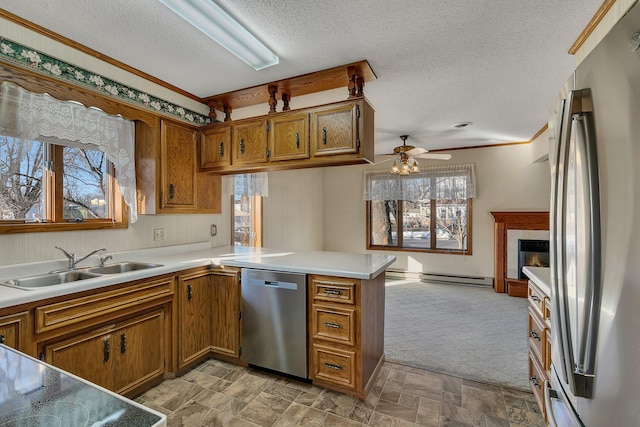 kitchen featuring brown cabinetry, stone finish floor, appliances with stainless steel finishes, a peninsula, and a sink