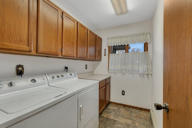 laundry room featuring cabinet space, baseboards, stone finish floor, a textured ceiling, and washing machine and dryer