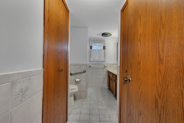 bathroom featuring a textured ceiling, tile patterned flooring, toilet, vanity, and tile walls