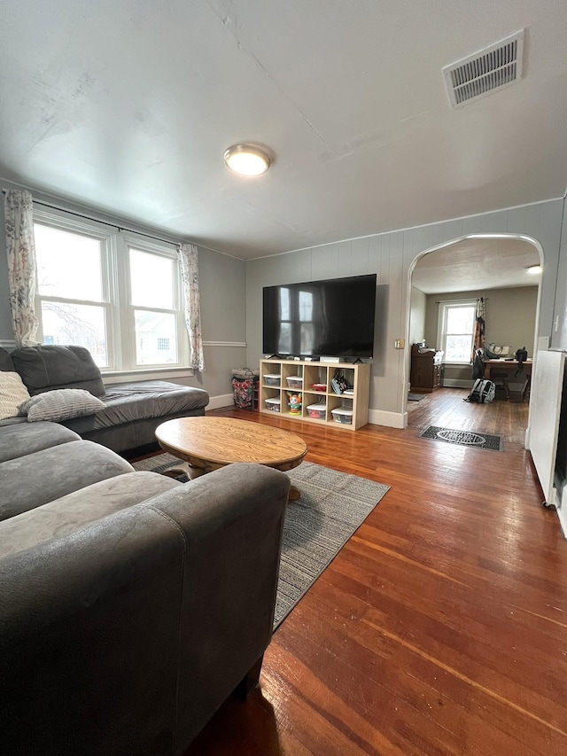 living room featuring arched walkways, visible vents, baseboards, and wood finished floors