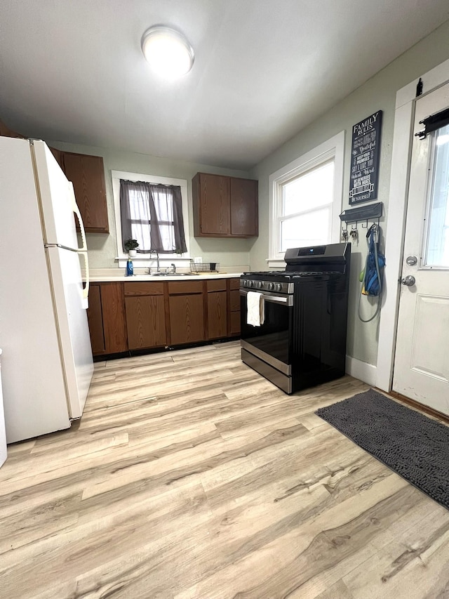 kitchen featuring stainless steel gas range oven, a sink, light countertops, freestanding refrigerator, and light wood finished floors