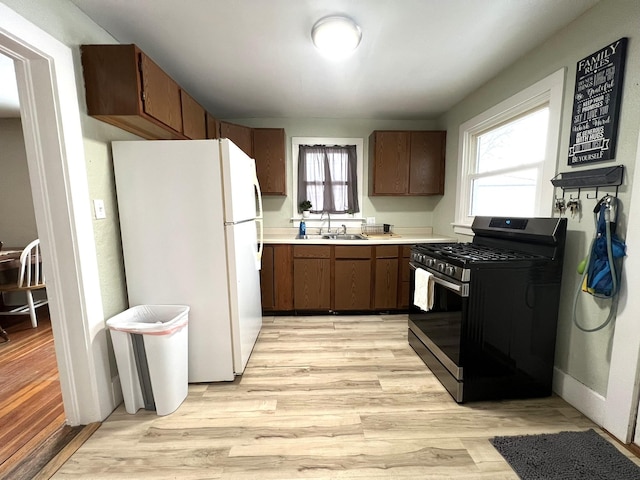 kitchen with light wood finished floors, light countertops, freestanding refrigerator, stainless steel gas stove, and a sink