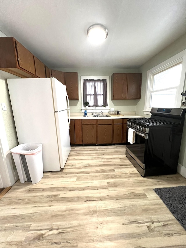 kitchen with a sink, light wood-style floors, light countertops, freestanding refrigerator, and gas range