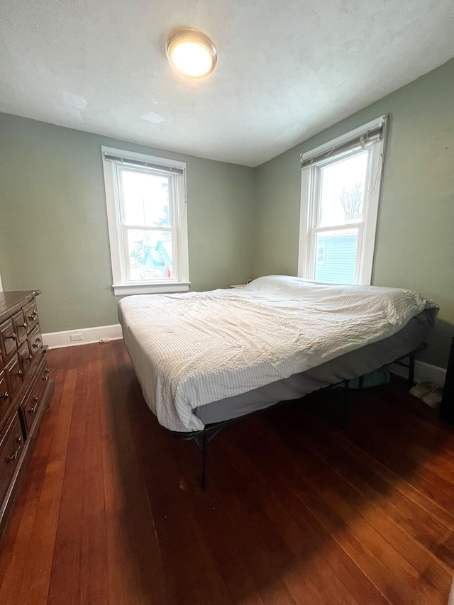 bedroom with multiple windows, dark wood-style flooring, and baseboards