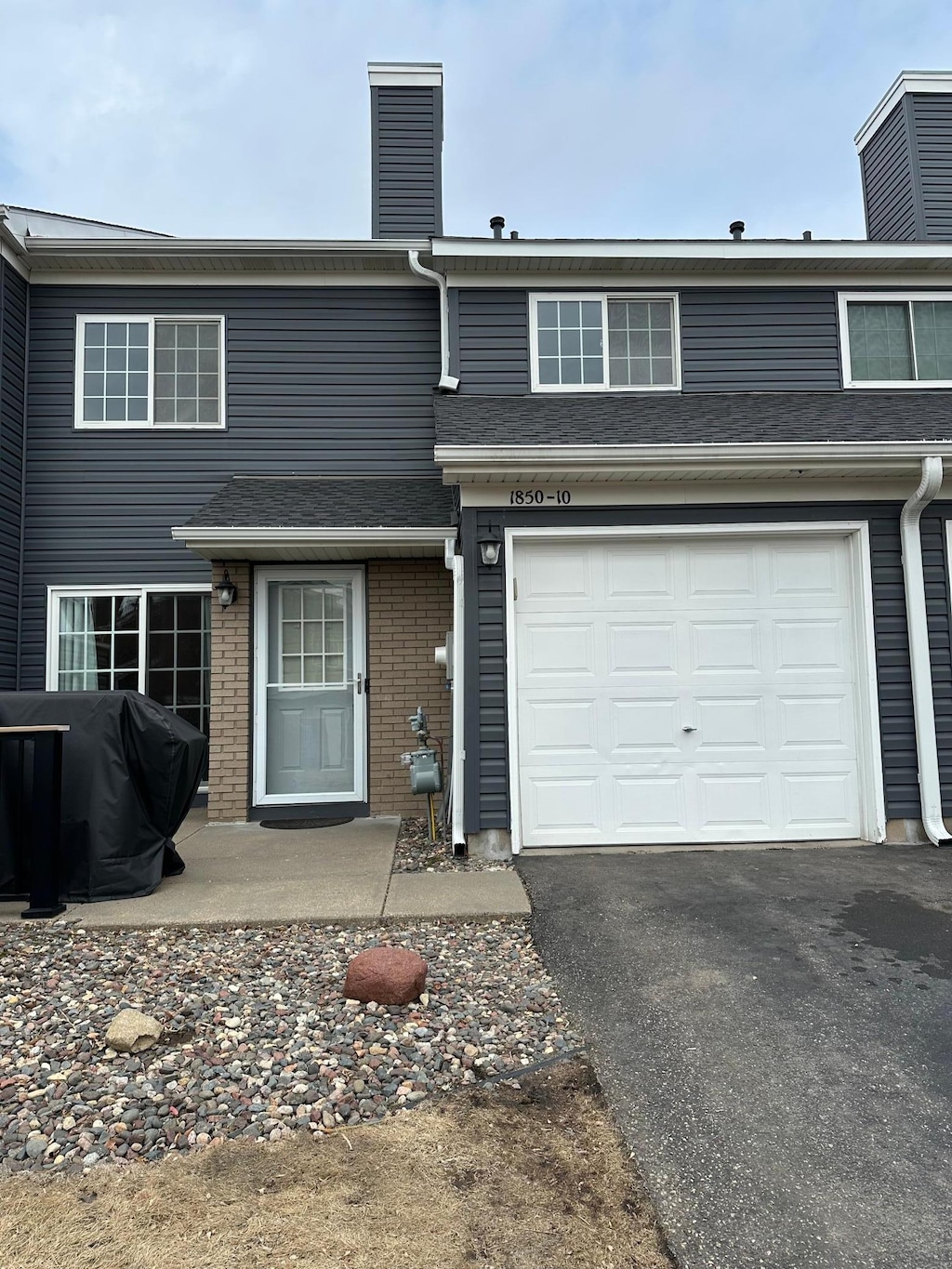 townhome / multi-family property featuring a garage, brick siding, driveway, and a chimney