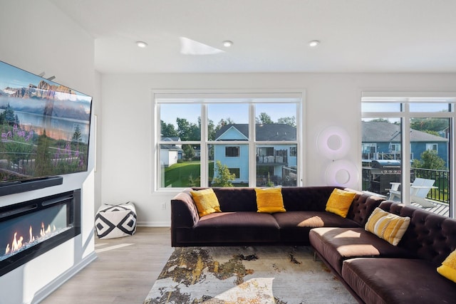 living area featuring light wood finished floors, recessed lighting, baseboards, and a glass covered fireplace