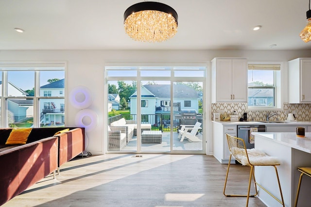 kitchen featuring white cabinetry, light wood-style floors, light countertops, stainless steel dishwasher, and decorative backsplash