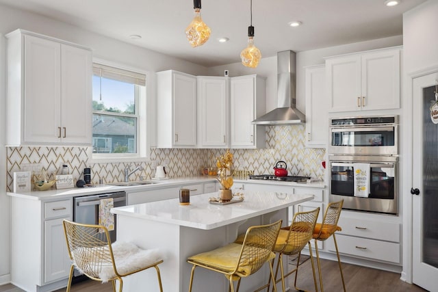 kitchen featuring a sink, white cabinetry, a kitchen breakfast bar, wall chimney range hood, and appliances with stainless steel finishes