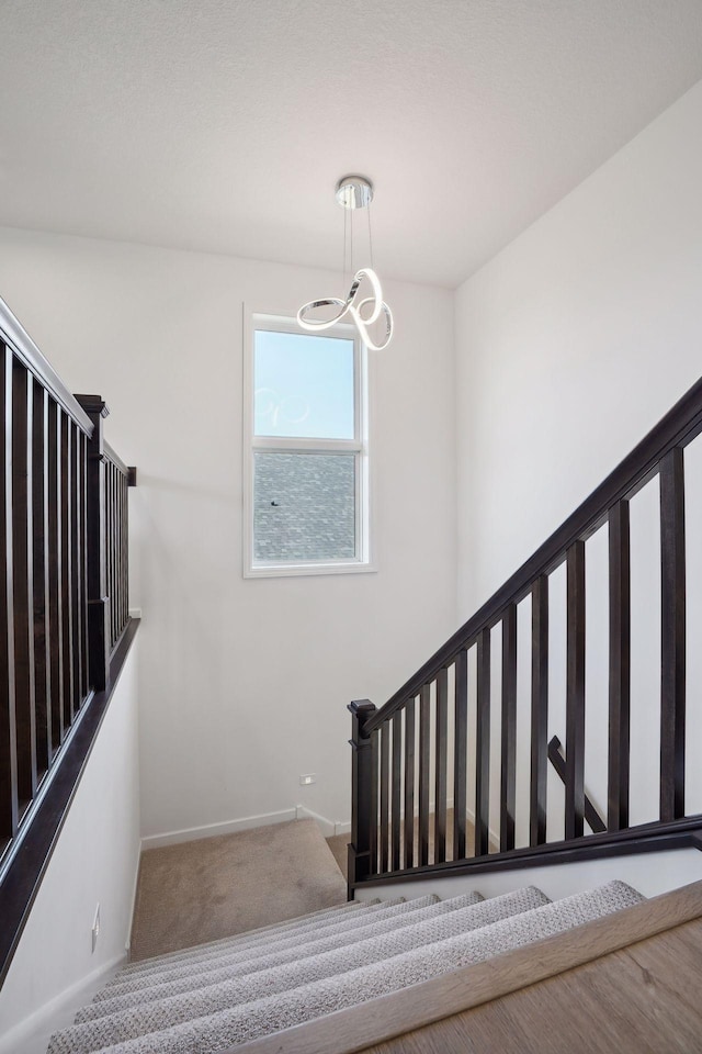 stairs with a chandelier, carpet, and baseboards