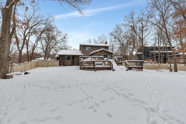 snow covered rear of property with a deck, a chimney, and fence