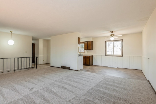 unfurnished living room with a wainscoted wall, light colored carpet, and a ceiling fan