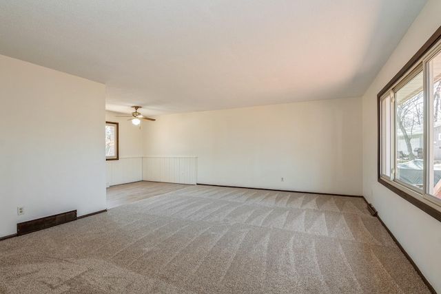 unfurnished room featuring a wainscoted wall, carpet flooring, visible vents, and ceiling fan