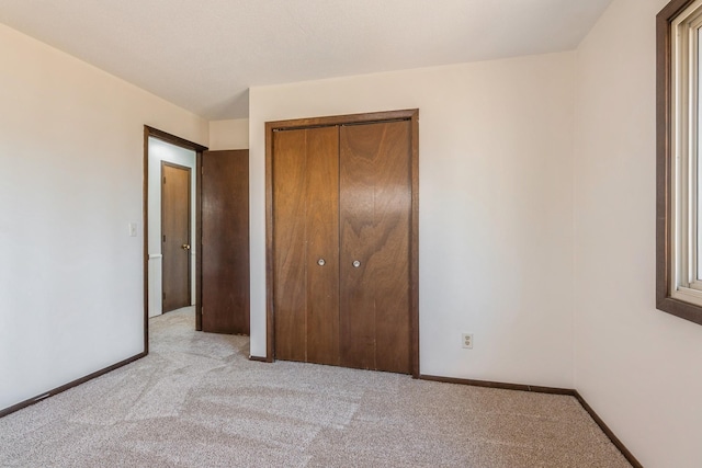 unfurnished bedroom featuring a closet, baseboards, and light colored carpet