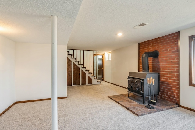 finished below grade area featuring visible vents, stairs, a wood stove, and carpet floors