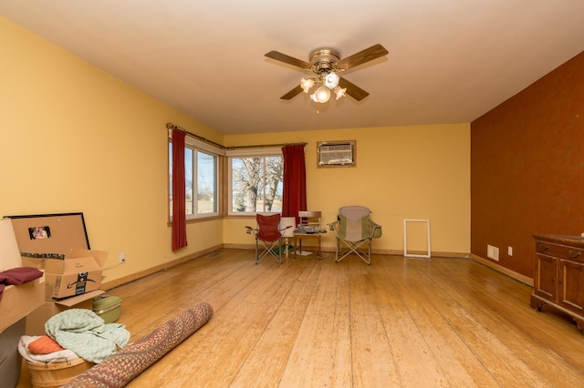 sitting room featuring a wall unit AC, baseboards, ceiling fan, and light wood finished floors