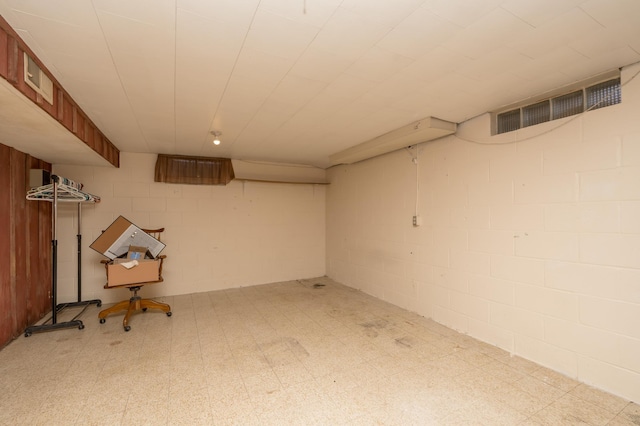 finished basement with concrete block wall, visible vents, and tile patterned floors